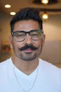 Close-up portrait of a middle-aged man with styled mustache and glasses indoors.